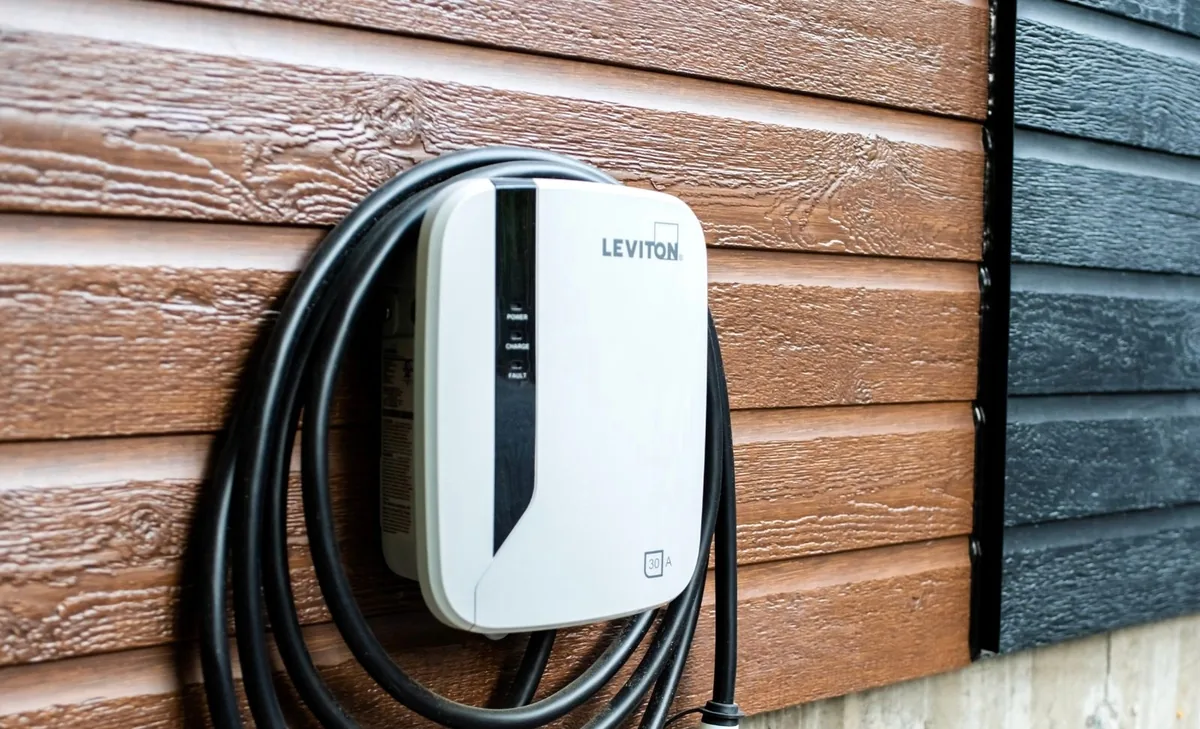 Leviton EV charger mounted on brown wood siding, with the charging cable coiled on the unit
